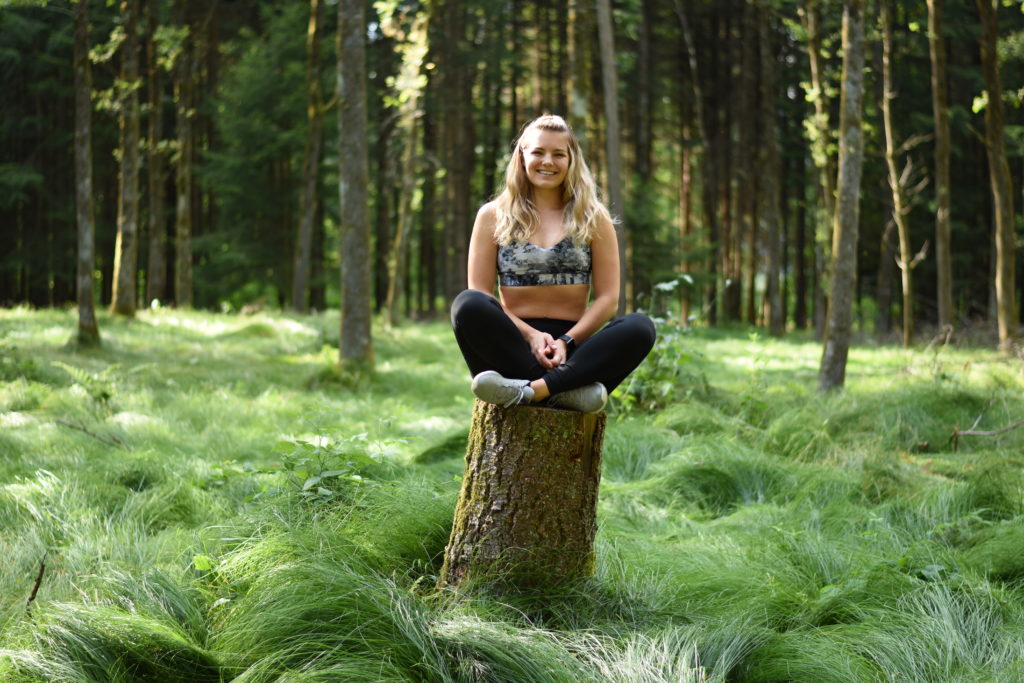 Viviane im Schneidersitz auf einem Baumstrunk im Wald